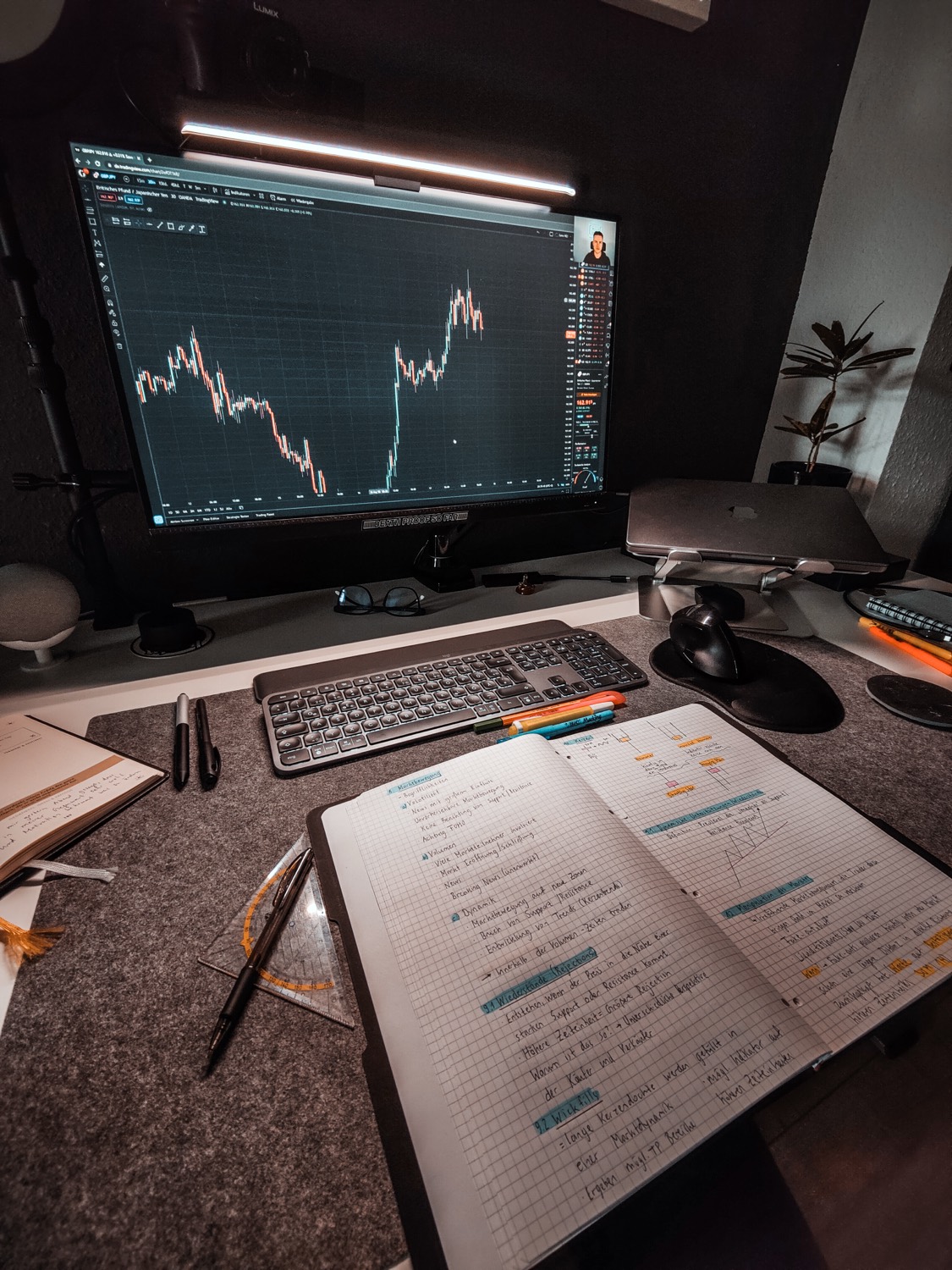 My desk while learning to trade by hand: a live chart on the monitor and a notebook full of handwritten trading notes.
